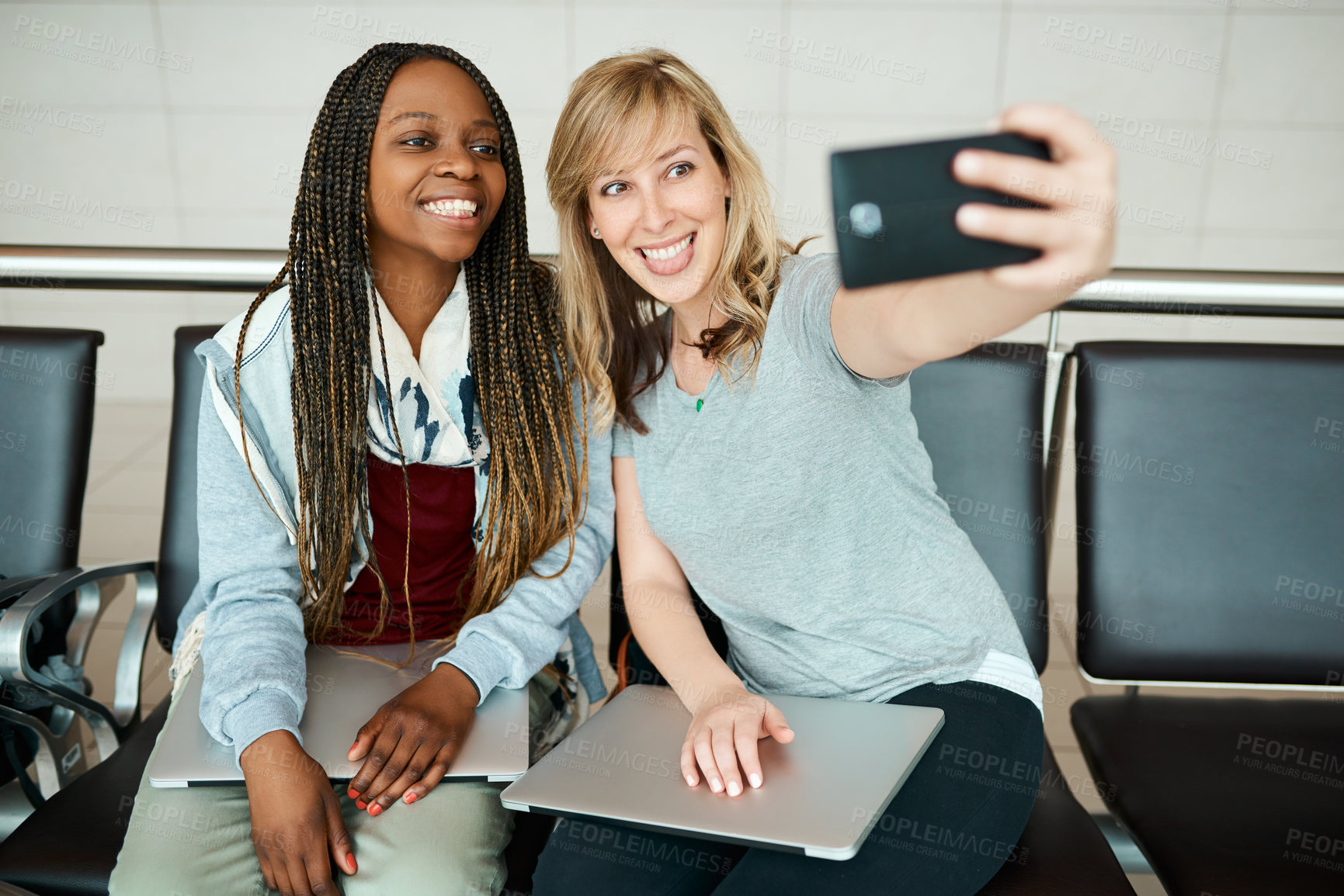 Buy stock photo Cropped shot of two young girlfriends taking selfies in the departure lounge of an airport