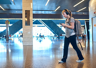 Buy stock photo Full length shot of an attractive young woman sending a text while walking through an airport