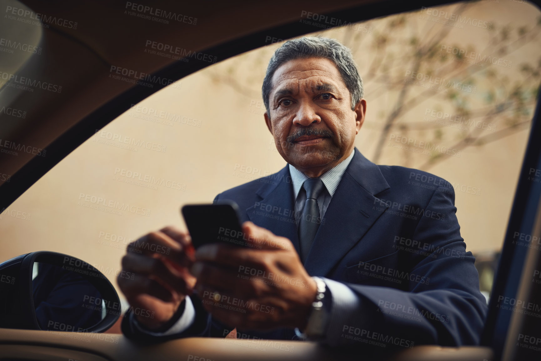 Buy stock photo Shot of a mature businessman using a phone while leaning against his car