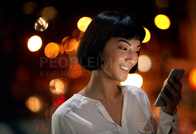 Buy stock photo Shot of an attractive young woman using a mobile phone outside in the city at night