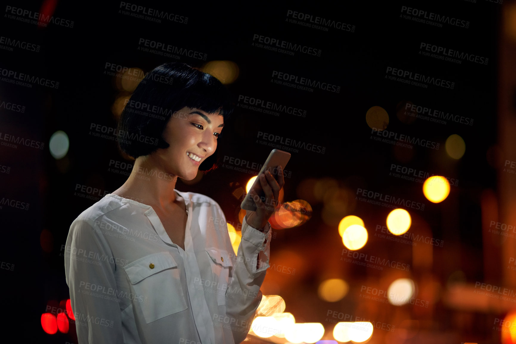 Buy stock photo Shot of an attractive young woman using a mobile phone outside in the city at night