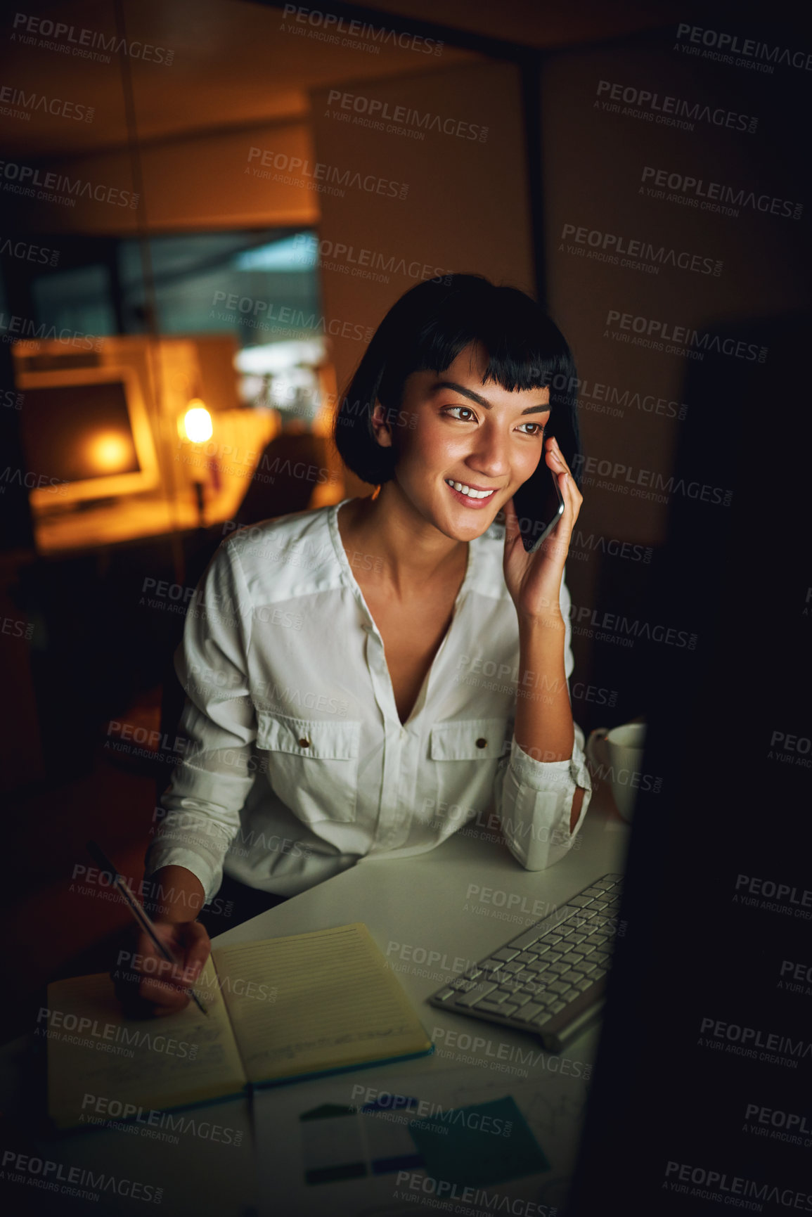Buy stock photo Shot of a young businesswoman using a mobile phone and computer during a late night at work