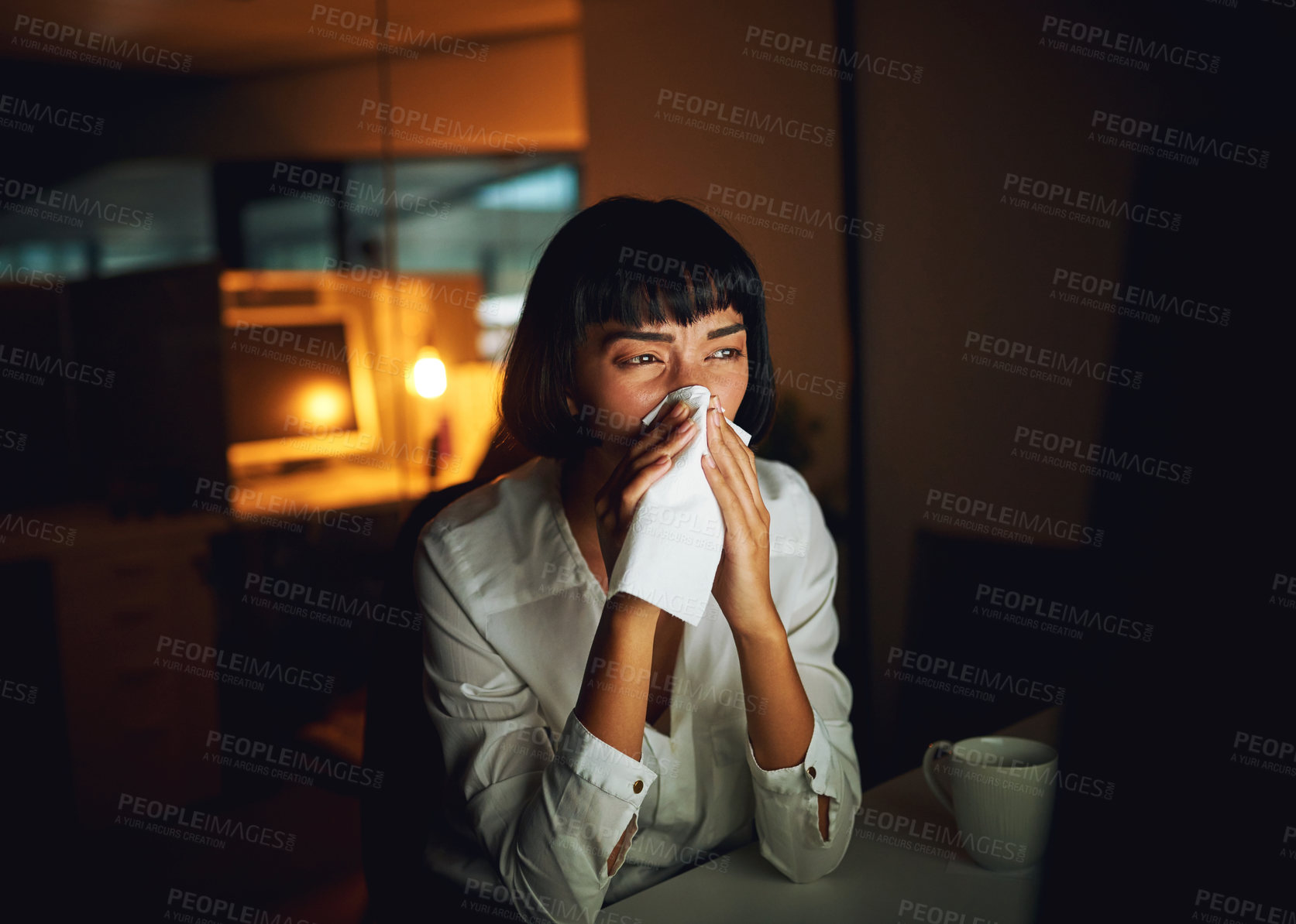Buy stock photo Shot of a young businesswoman blowing her nose during a late night at work