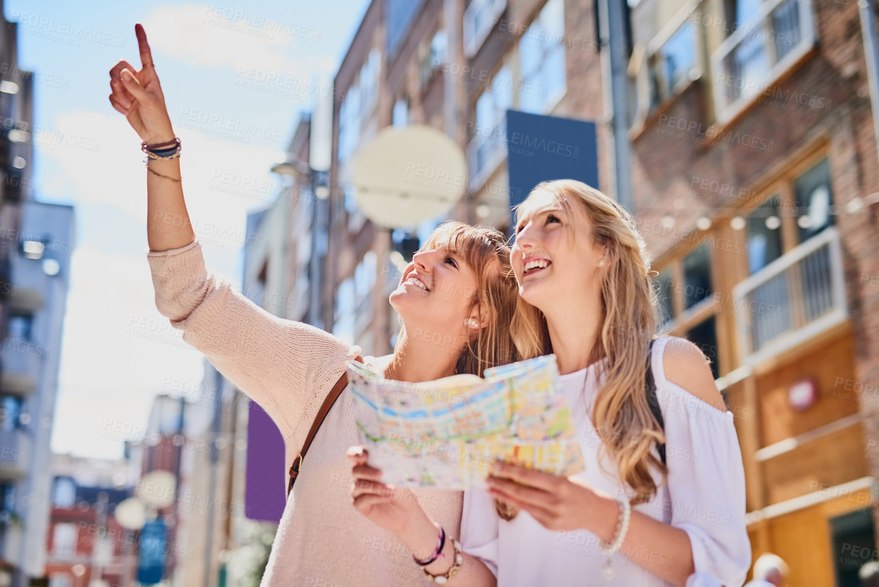 Buy stock photo Low angle shot of two attractive young girlfriends reading a map while exploring a foreign city