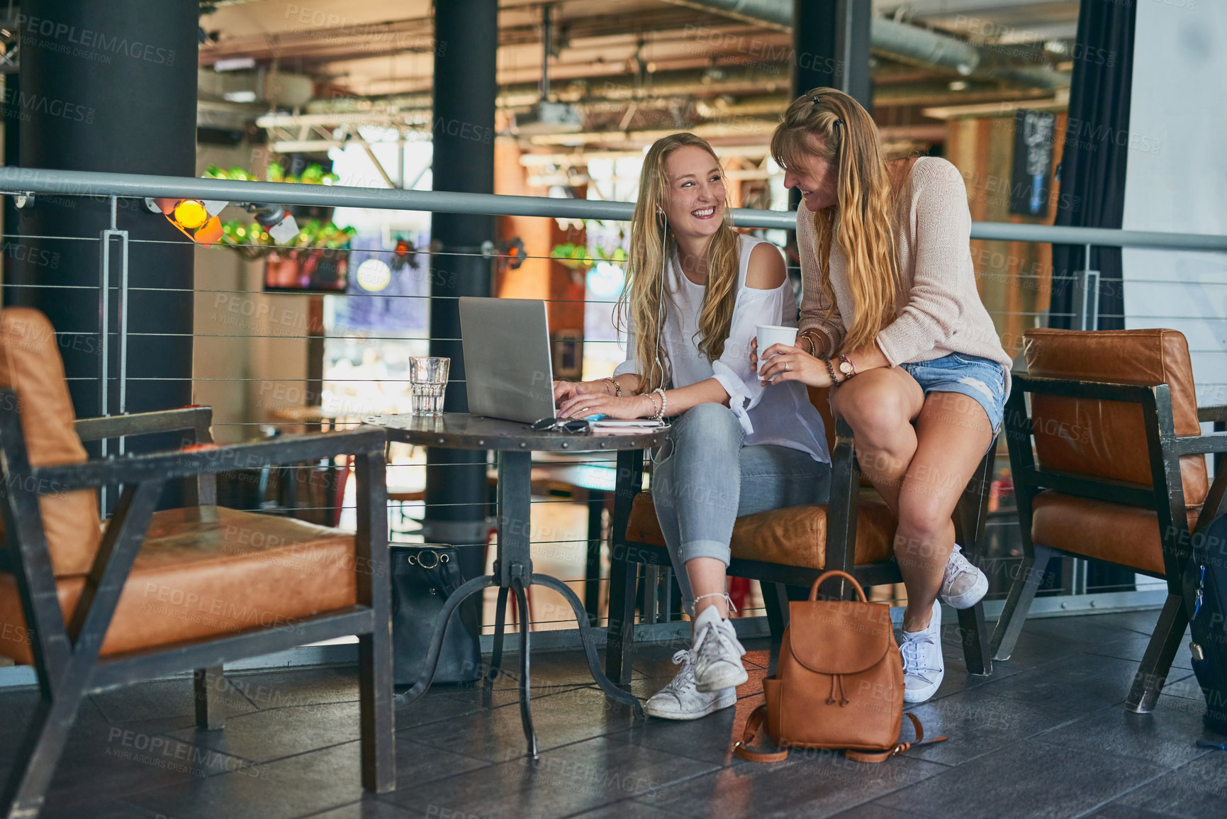 Buy stock photo Full length shot of a two attractive young friends using a laptop while sitting in a cafe