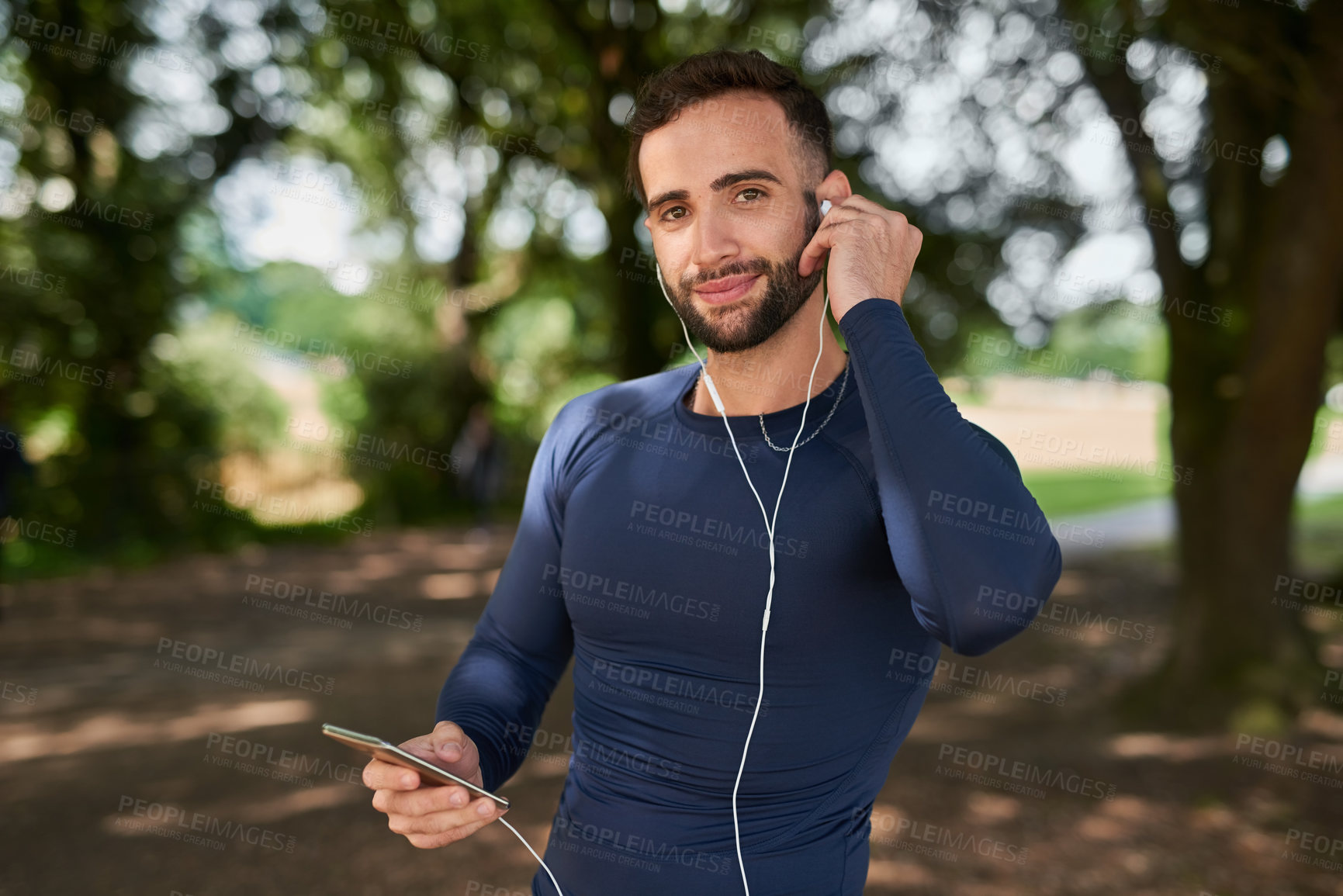 Buy stock photo Man, runner and phone with earphones in portrait at park, smile and exercise with audio streaming app. Person, happy and smartphone with online subscription for listening to music at training on path