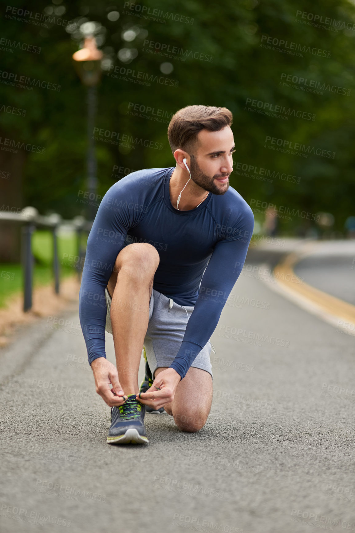 Buy stock photo Full length shot of a handsome young male runner tying his shoelaces during an outdoor workout