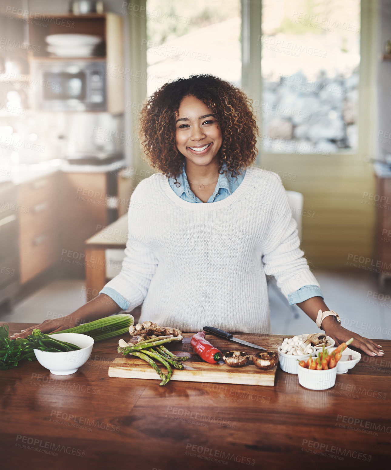 Buy stock photo Portrait of happy black woman preparing healthy food in a kitchen at home. Young African American using fresh vegetables to make a delicious, balanced low carb meal. Lady on a cleanse and detox diet 