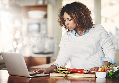 Buy stock photo Shot of a young woman using a laptop while preparing a healthy meal at home
