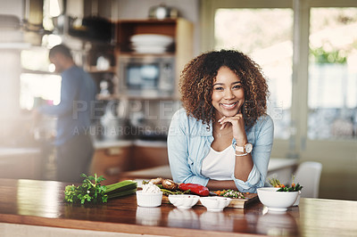 Buy stock photo Portrait of a happy, healthy and carefree young woman preparing a healthy meal at home with her husband in the background. Black wife making an organic vegetarian salad for lunch in a kitchen