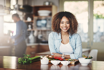 Buy stock photo Portrait of a happy young woman preparing a healthy meal at home with her husband in the background