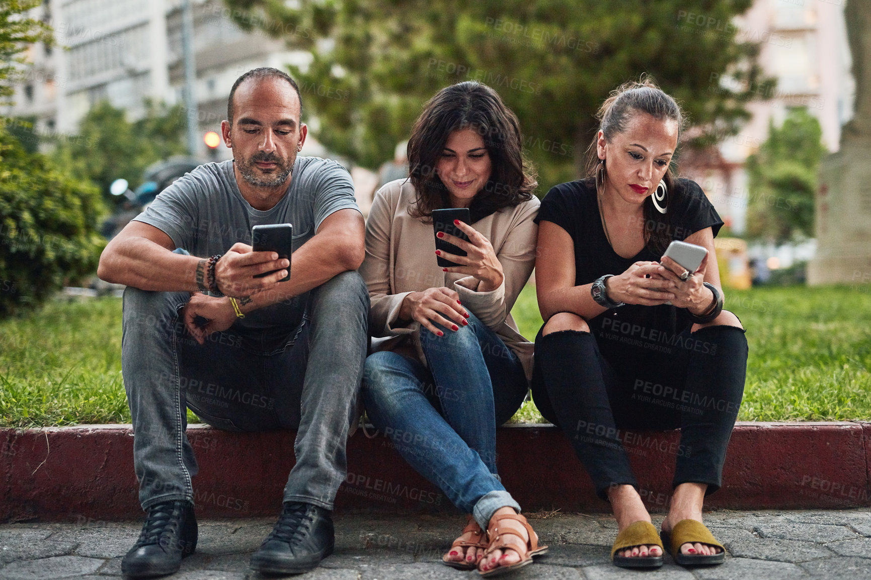 Buy stock photo Shot of three friends using their cellphones while spending time together in the city