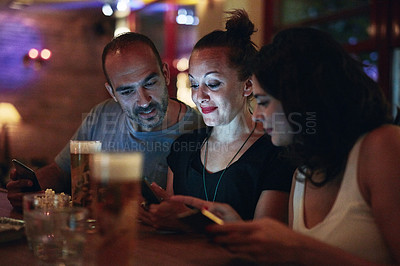 Buy stock photo Shot of friends looking at something on a cellphone while sitting in the club