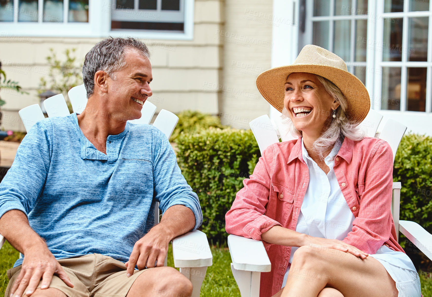 Buy stock photo Mature couple, lawn and relax on chair with funny conversation, bonding and care in summer at house. Man, woman and happy with laughing at comic memory, talking or chat on grass in backyard garden