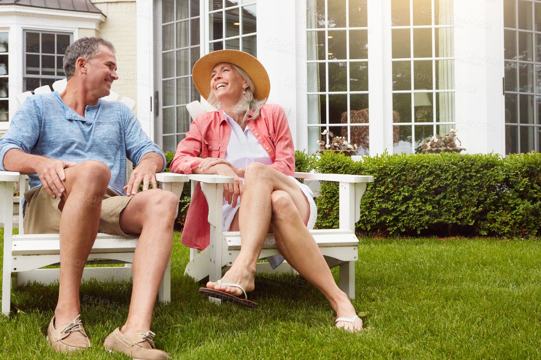 Buy stock photo Mature couple, garden and talking on chair with funny conversation, bonding and care in summer at house. Man, woman and happy with laughing at retirement, relax and chat on grass in home backyard