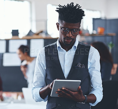 Buy stock photo Cropped shot of a handsome young businessman using a tablet in the office with his colleagues in the background