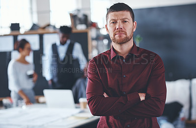Buy stock photo Cropped portrait of a handsome young businessman standing with his arms folded with his colleagues in the background
