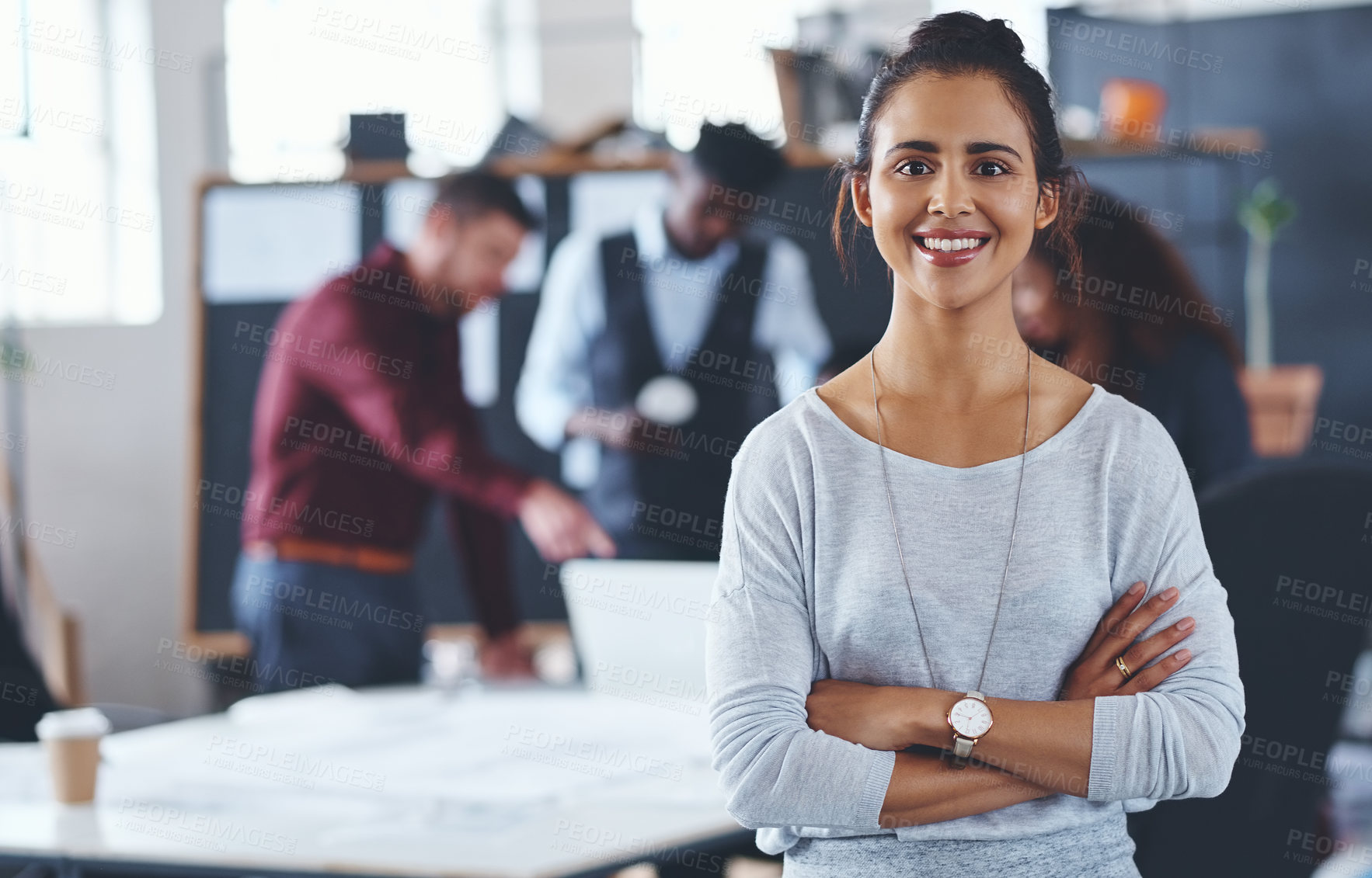 Buy stock photo Cropped portrait of an attractive young businesswoman standing with her arms folded with her colleagues in the background