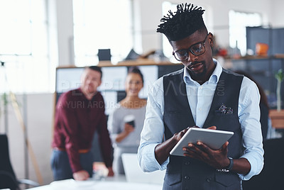 Buy stock photo Cropped shot of a handsome young businessman using a tablet in the office with his colleagues in the background