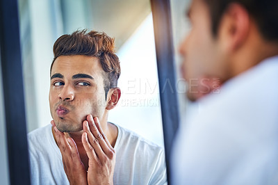 Buy stock photo Shot of a handsome young man admiring looking at his face in the bathroom mirror