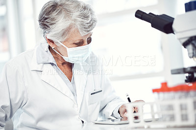 Buy stock photo Shot of a focused elderly female scientist working and making notes while wearing a doctor's mask inside of a laboratory