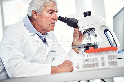 Buy stock photo Shot of a focused elderly male scientist looking through a microscope while being seated inside of a laboratory