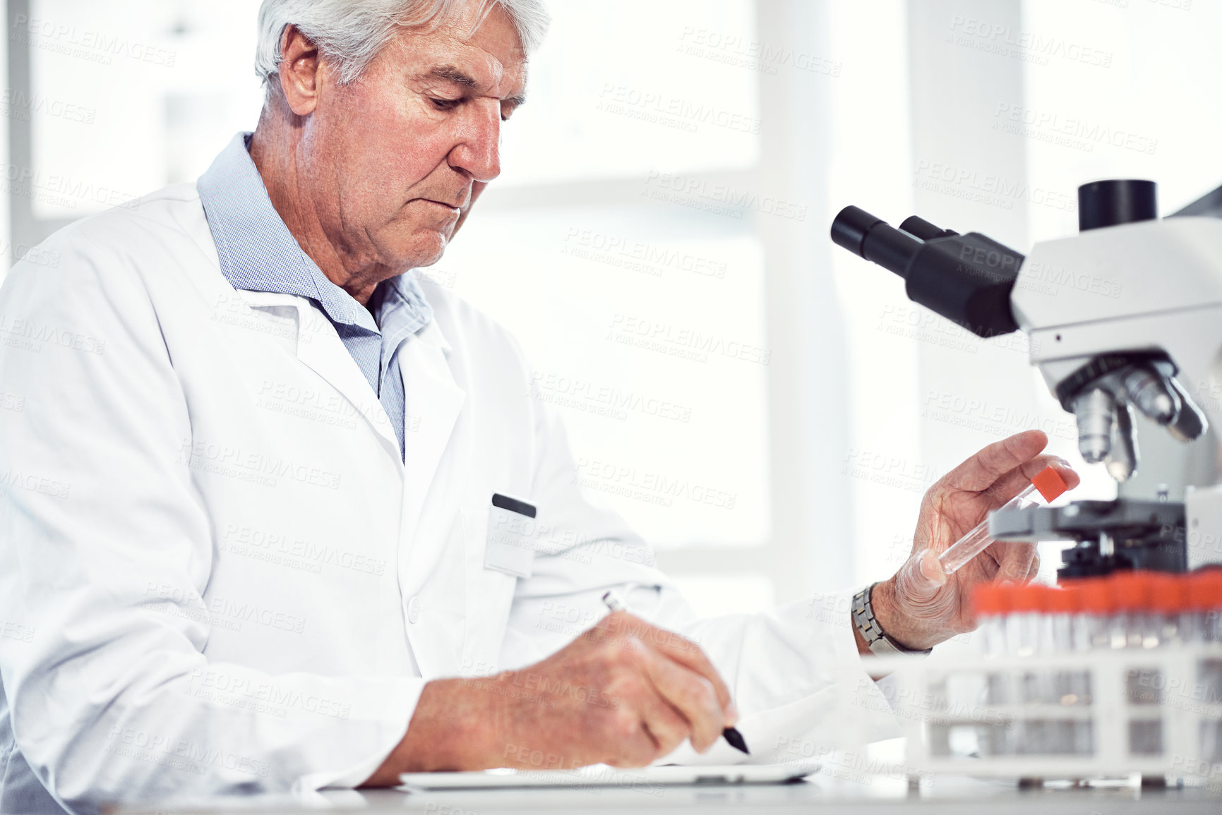 Buy stock photo Shot of a focused elderly male scientist holding up a test tube and making notes while being seated inside of a laboratory