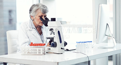 Buy stock photo Shot of a focused elderly female scientist looking through a microscope while being seated in a laboratory
