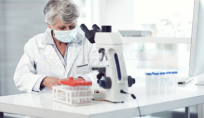 Buy stock photo Shot of a focused elderly female scientist working and making notes while wearing a doctor's mask inside of a laboratory