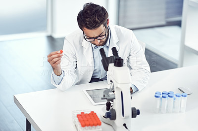 Buy stock photo Shot of a focused young male scientist making notes while holding up a test tube inside a laboratory