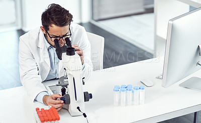 Buy stock photo Shot of a focused young male scientist looking through a microscope inside of a laboratory