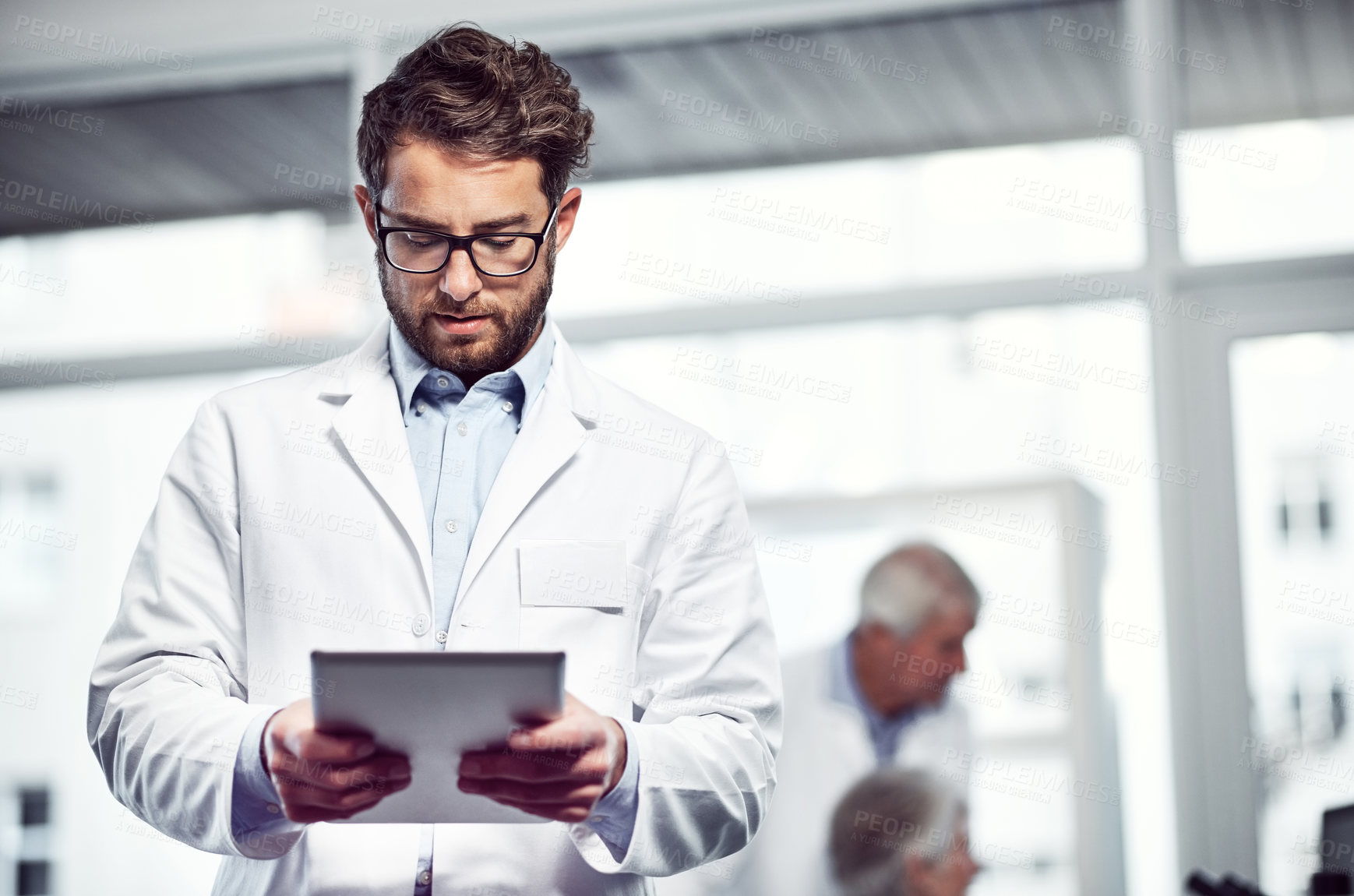 Buy stock photo Shot of a focused young male scientist using a digital tablet while standing inside of a laboratory
