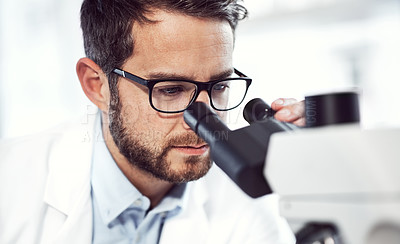 Buy stock photo Shot of a focused young male scientist looking through a microscope while being seated inside of a laboratory