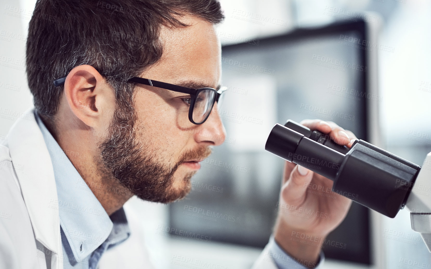 Buy stock photo Shot of a focused young male scientist looking through a microscope while being seated inside of a laboratory