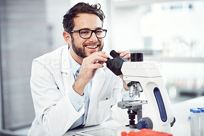 Buy stock photo Shot of a cheerful young male scientist looking through a microscope while being seated inside of a laboratory