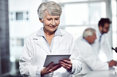 Buy stock photo Shot of a cheerful elderly female scientist using a digital tablet while standing inside of a laboratory