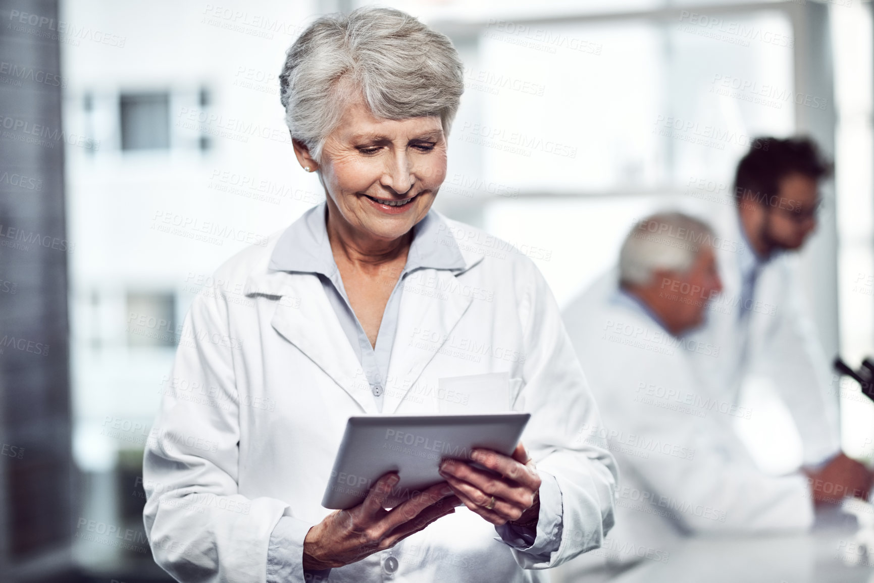 Buy stock photo Shot of a cheerful elderly female scientist using a digital tablet while standing inside of a laboratory