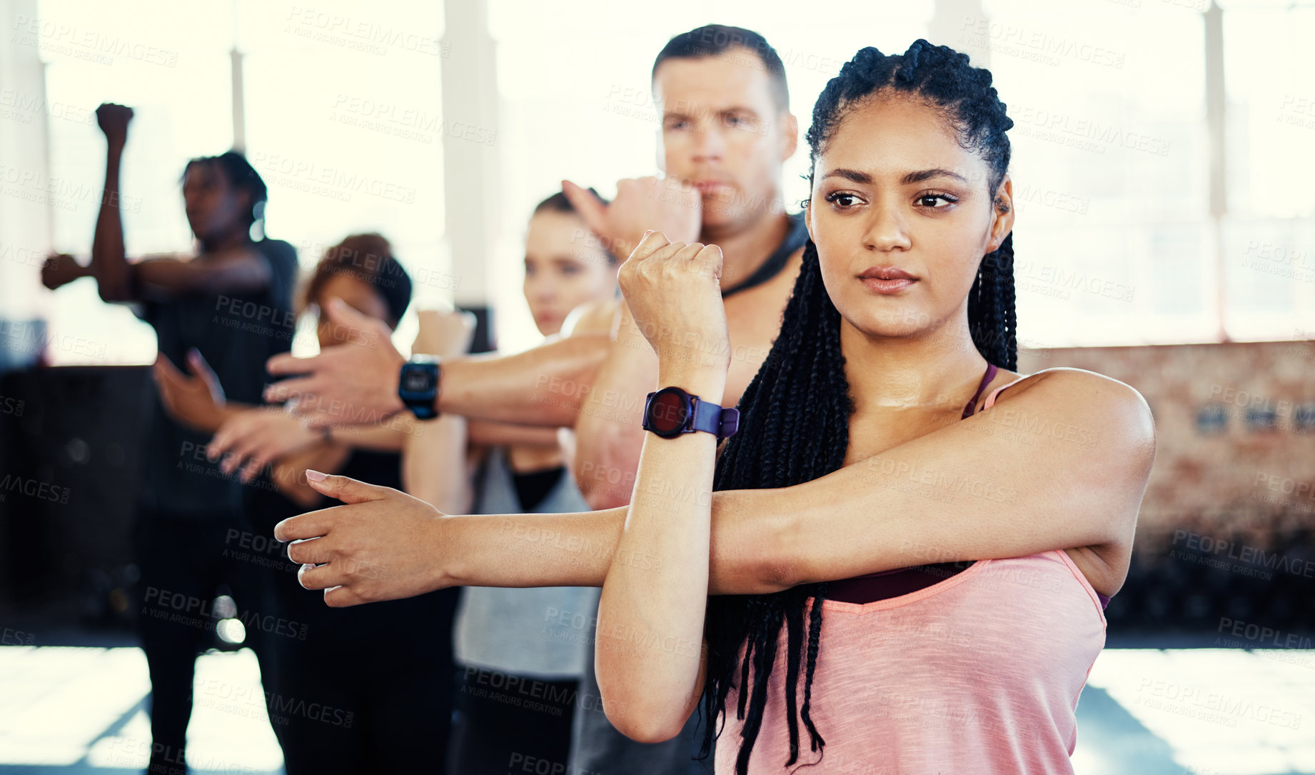 Buy stock photo Shot of a focused group of young people standing in a row and stretching before a workout session in a gym