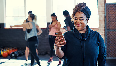Buy stock photo Shot of a cheerful young woman standing and using her cellphone before a workout session in a gym