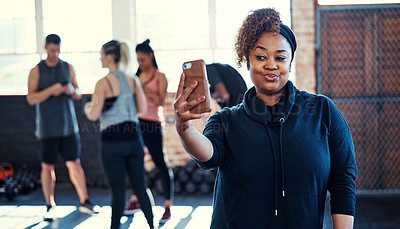 Buy stock photo Shot of a cheerful young woman standing and taking a self portrait with her cellphone before a workout in a gym