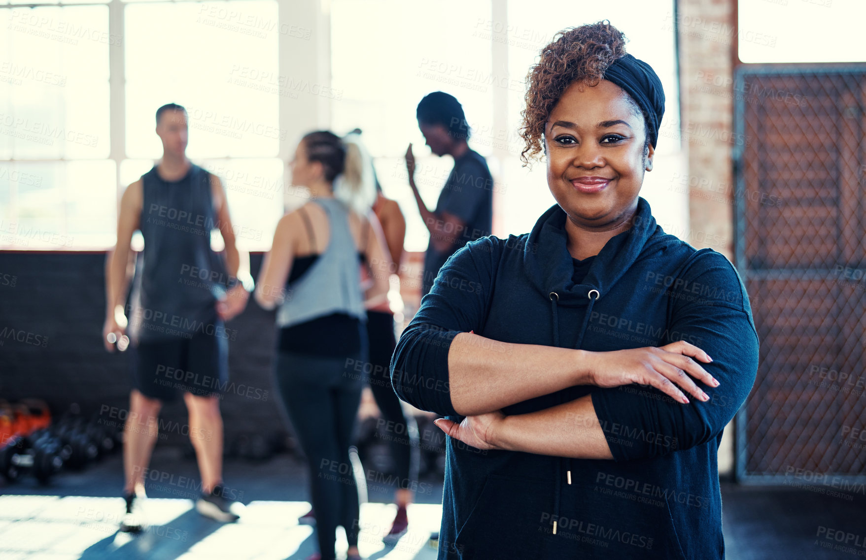 Buy stock photo Portrait of a cheerful young woman standing with her arms folded while looking into the camera before a workout in a gym