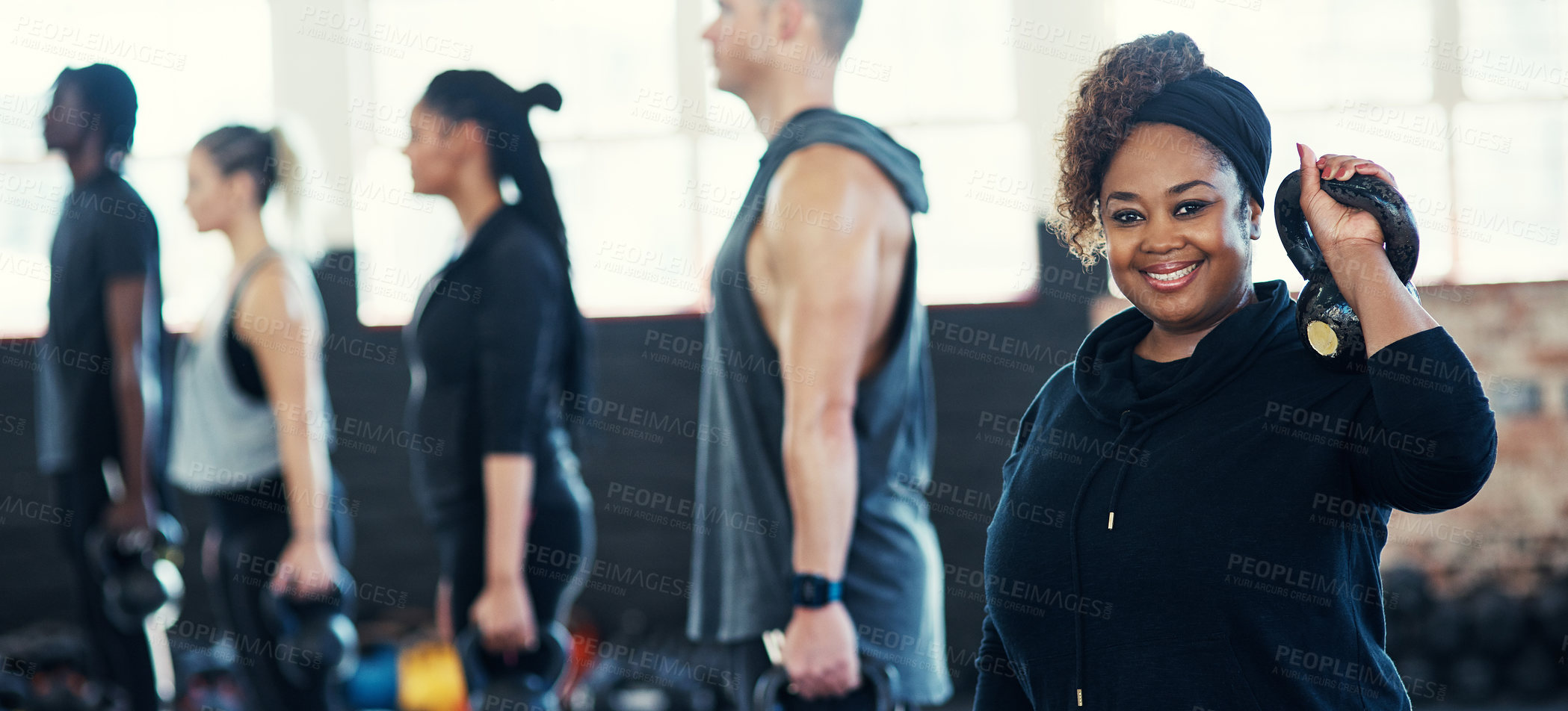 Buy stock photo Shot of a cheerful group of young people standing in a row and training with weights while one looks into the camera in a gym
