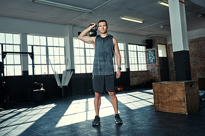 Buy stock photo Shot of a young man lifting kettlebells in a gym