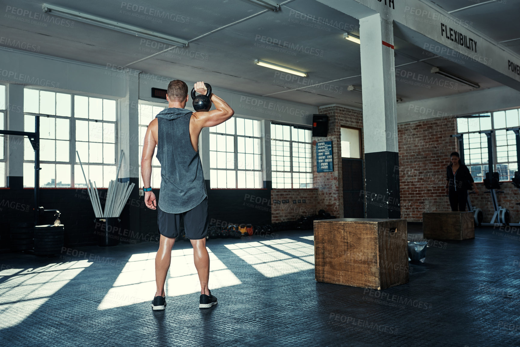 Buy stock photo Rearview shot of an unrecognizable man lifting kettlebells in a gym