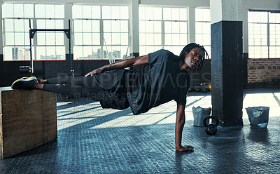 Buy stock photo Shot of a young man doing a side plank with a wooden block in a gym