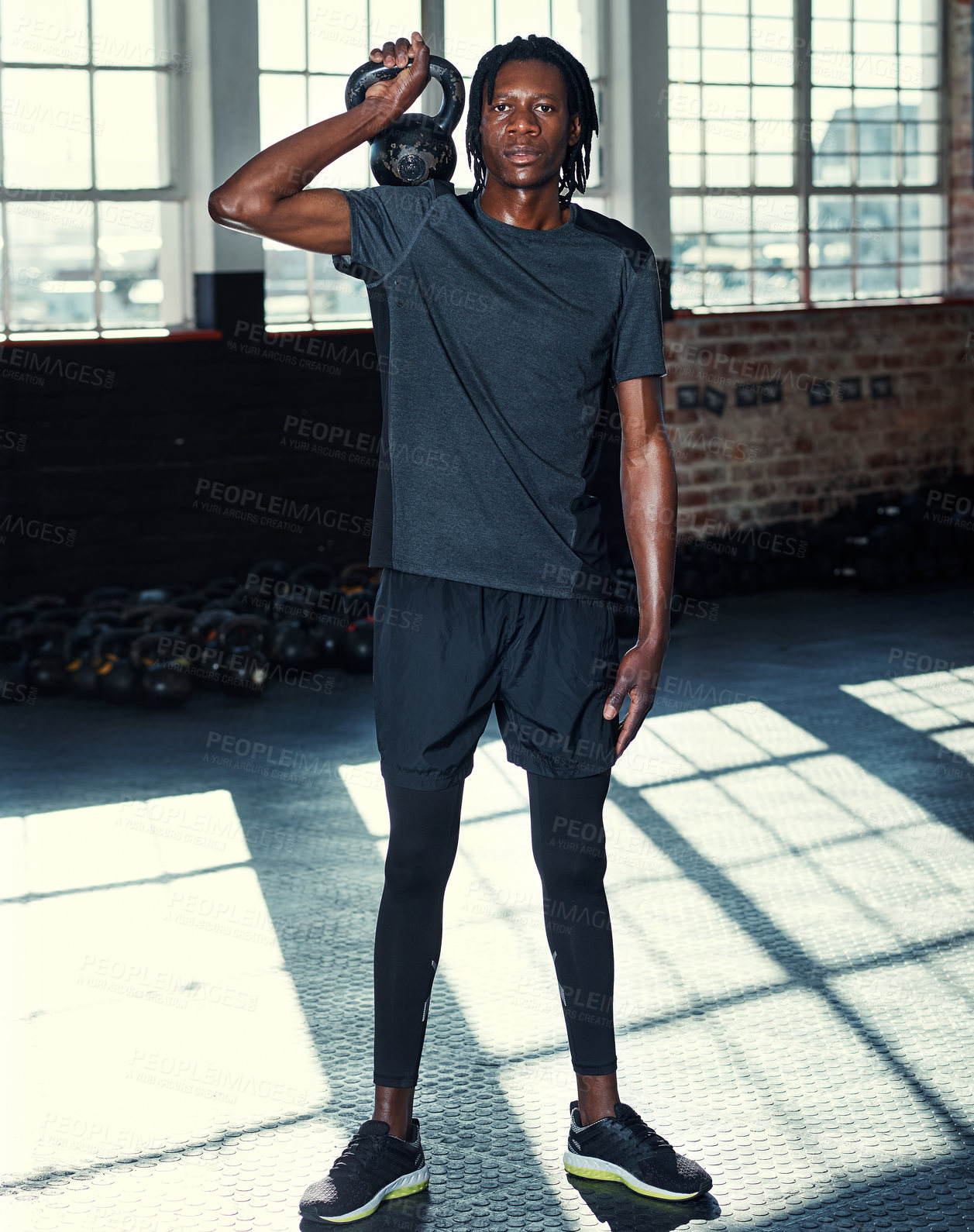 Buy stock photo Shot of a young man lifting kettlebells in a gym