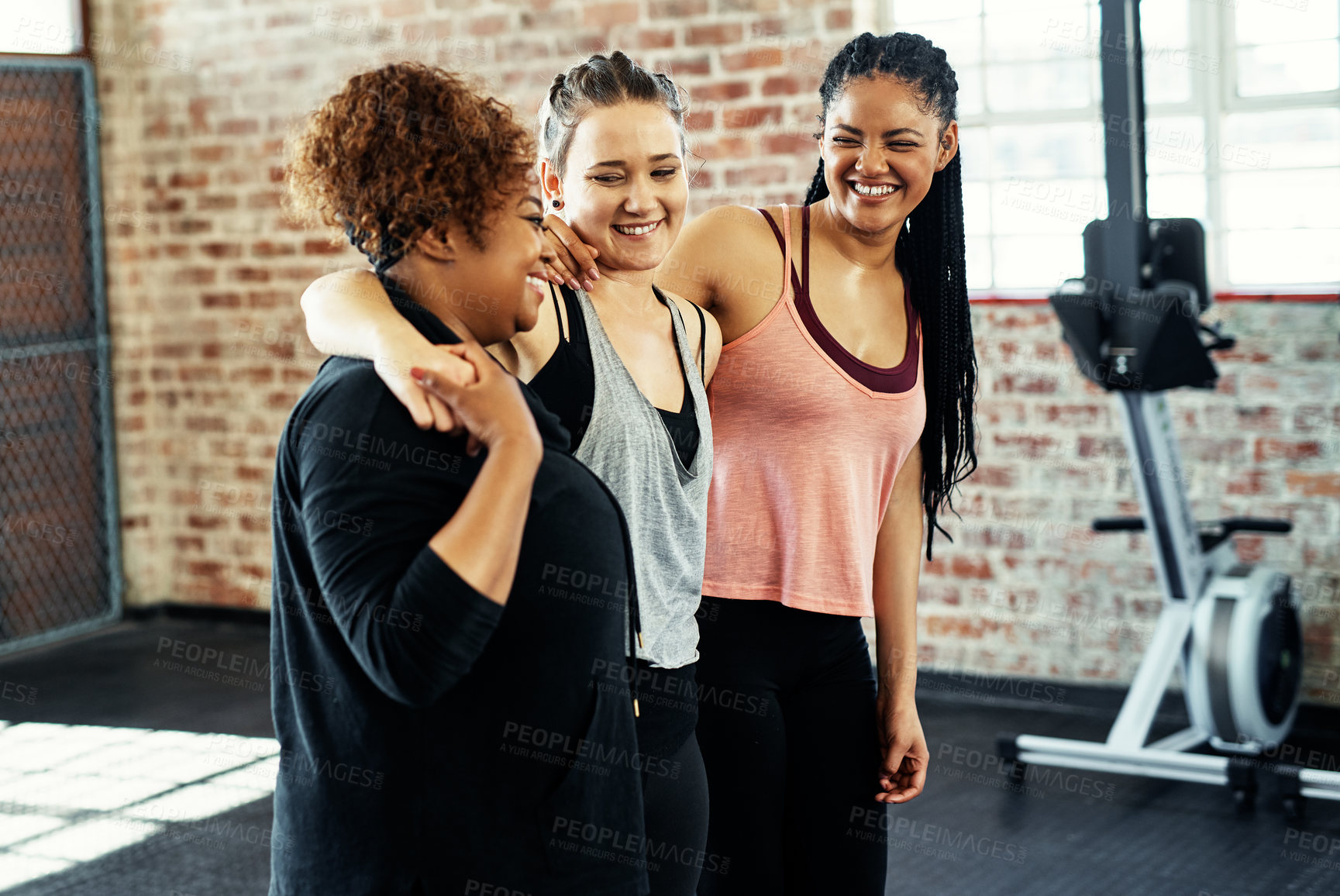 Buy stock photo Shot of three cheerful young women having a conversation while holding each other before a workout session in a gym