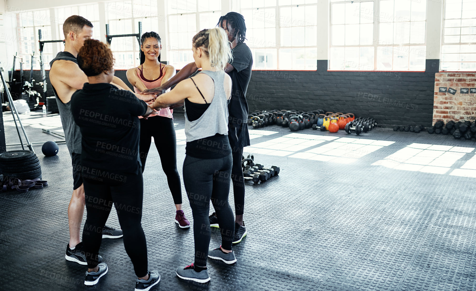 Buy stock photo Shot of a cheerful young group of people forming a huddle together while one looks at the camera before a workout session in a gym