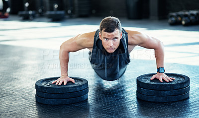Buy stock photo Shot of a young man doing push ups with weights in a gym