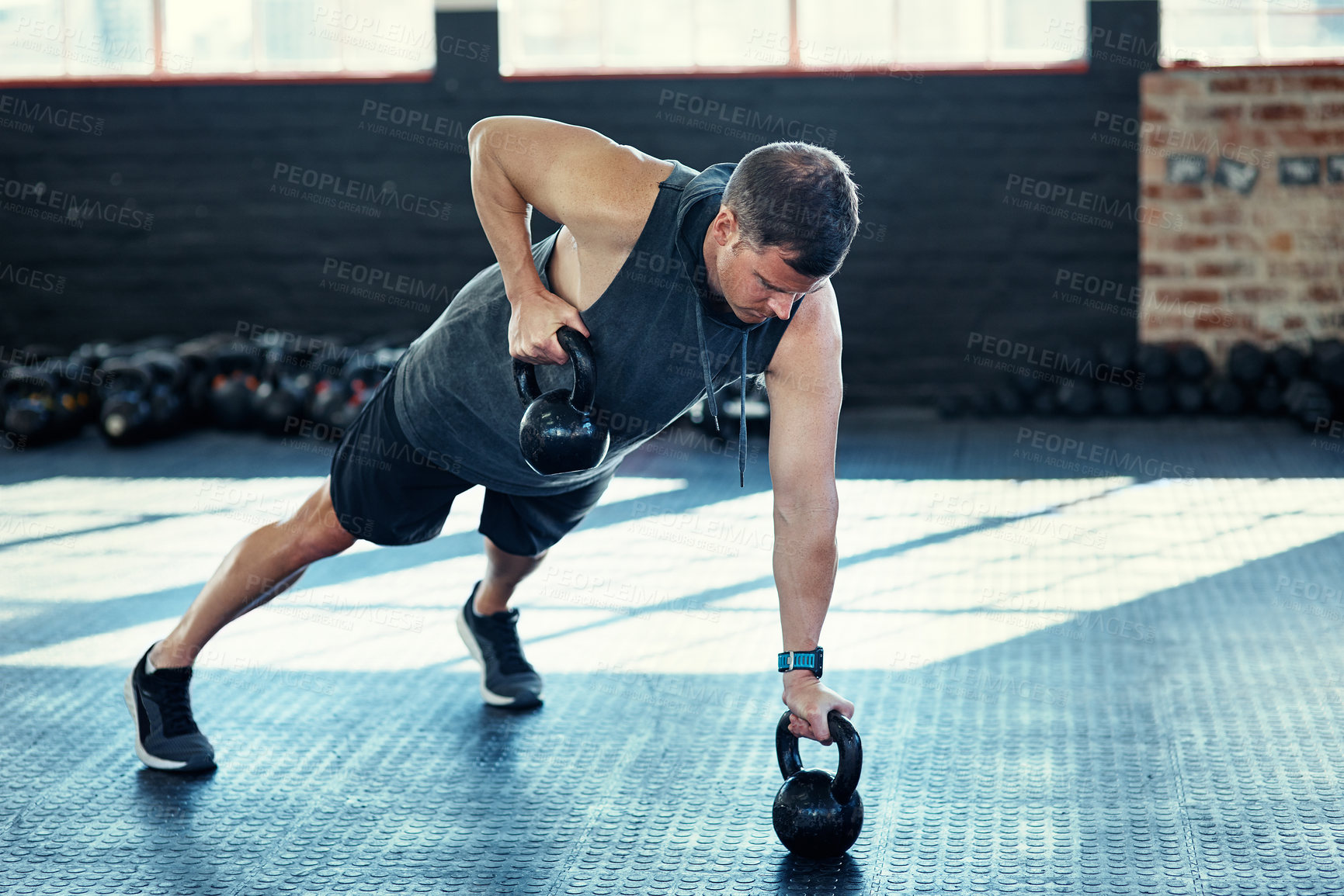 Buy stock photo Shot of a young man doing push ups with kettlebells in a gym